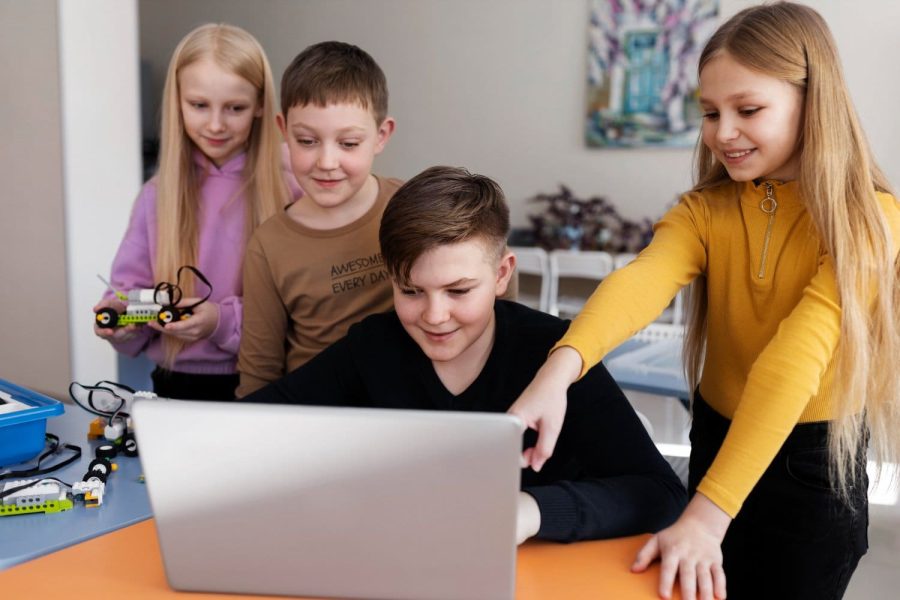 Four Children using a laptop and electronic parts to build a robot